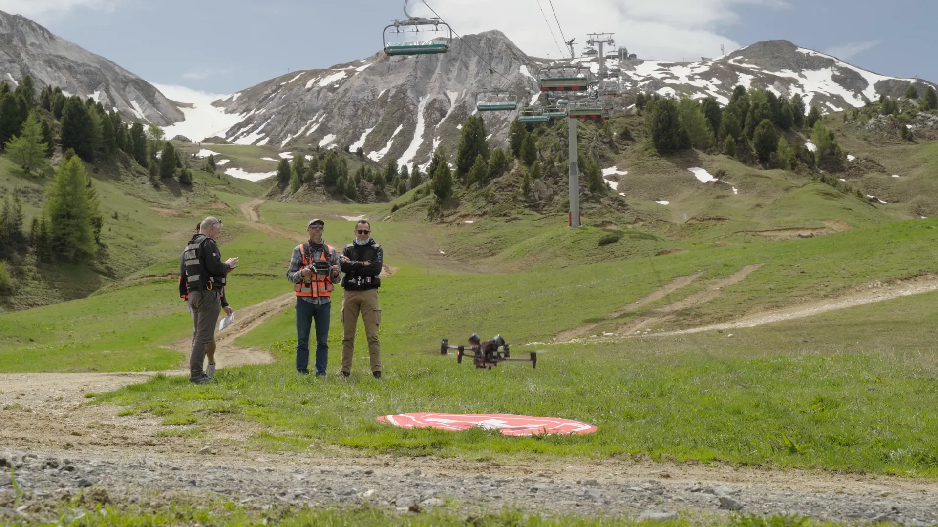 Trois télépilotes en formation sur une piste de ski en été, drone au sol