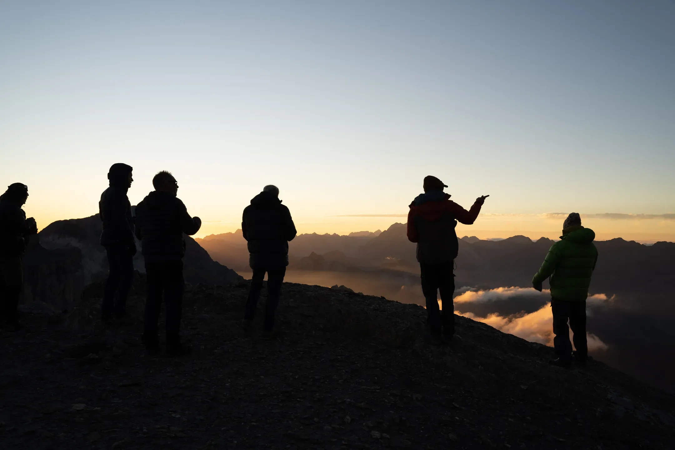 Silhouettes de l'équipe sur une crête au coucher du soleil, au-dessus d'une mer de nuages