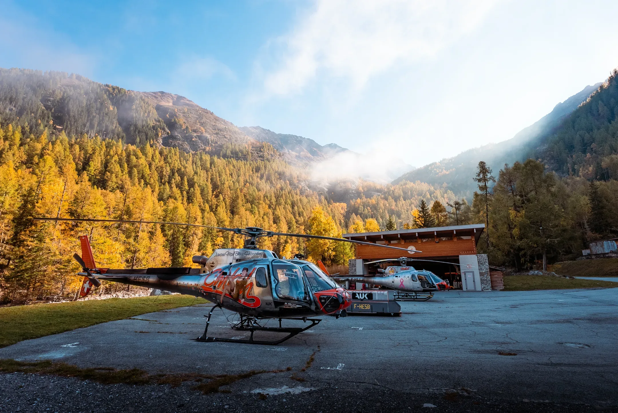 Hélicoptère sur son aire de décollage, forêt d'automne et montagnes dans la brume