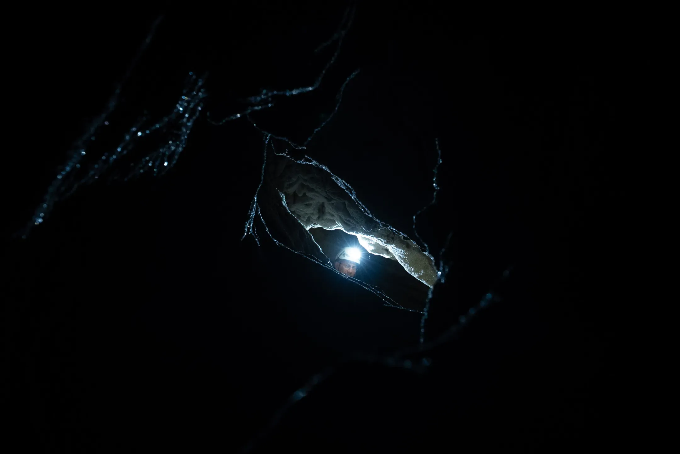 Un spéléologue à la lampe frontale apparaît dans une ouverture de la paroi, au milieu de l'obscurité