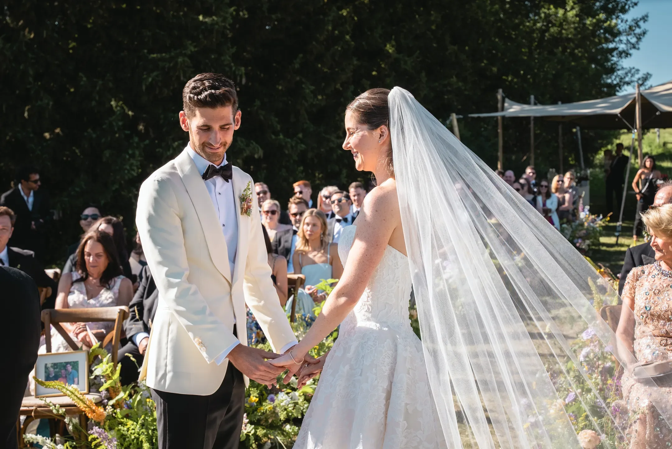 Le marié en veste blanche et la mariée voilée se regardent en souriant