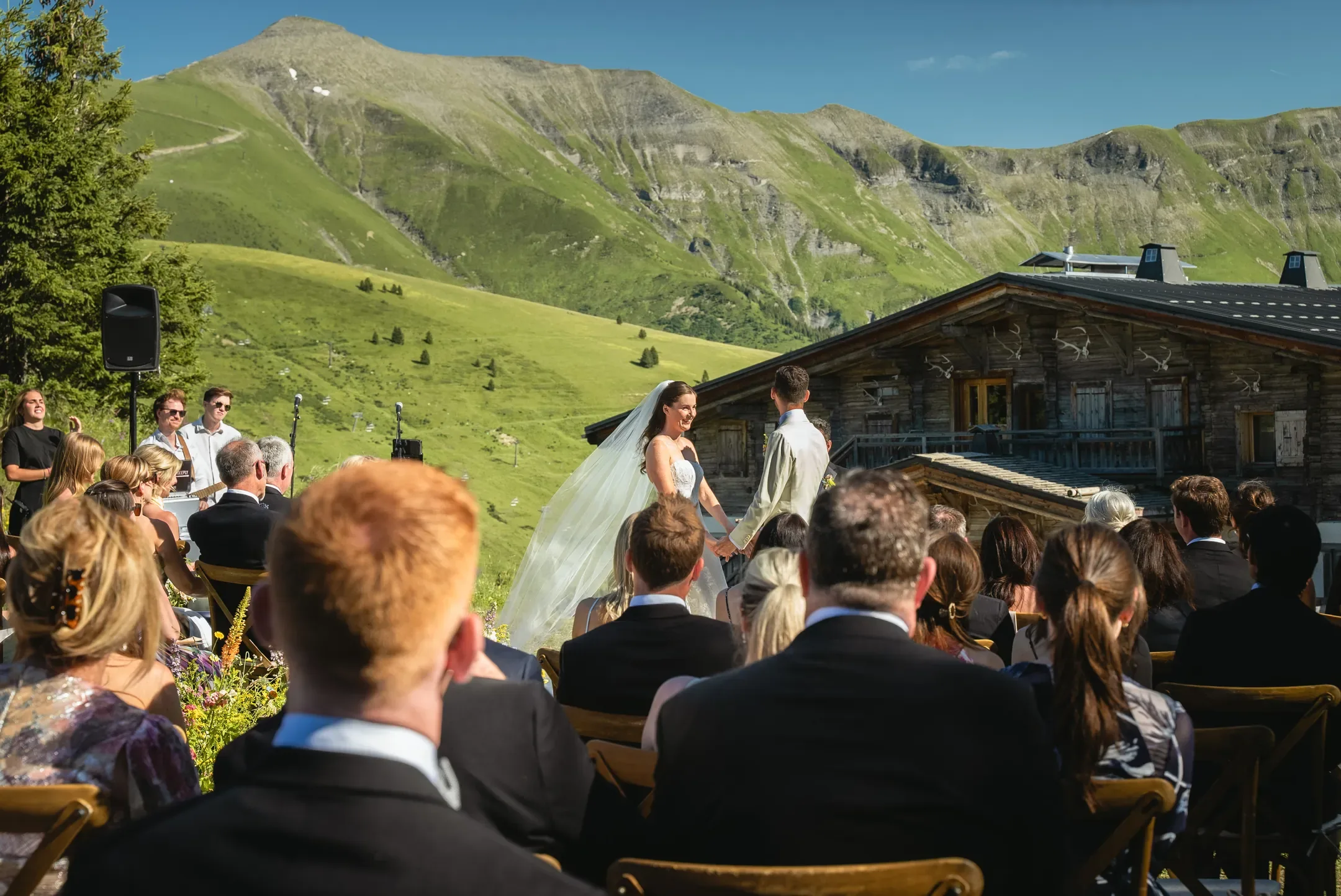 Invités assis devant un chalet d'alpage pendant la cérémonie
