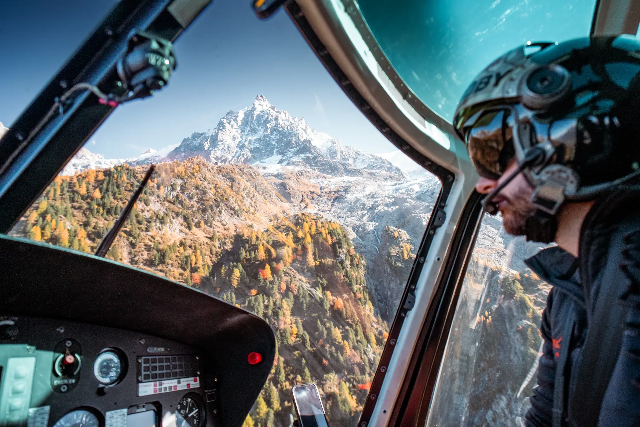 Pilote casqué dans le cockpit d'un hélicoptère, sommet enneigé à travers la verrière