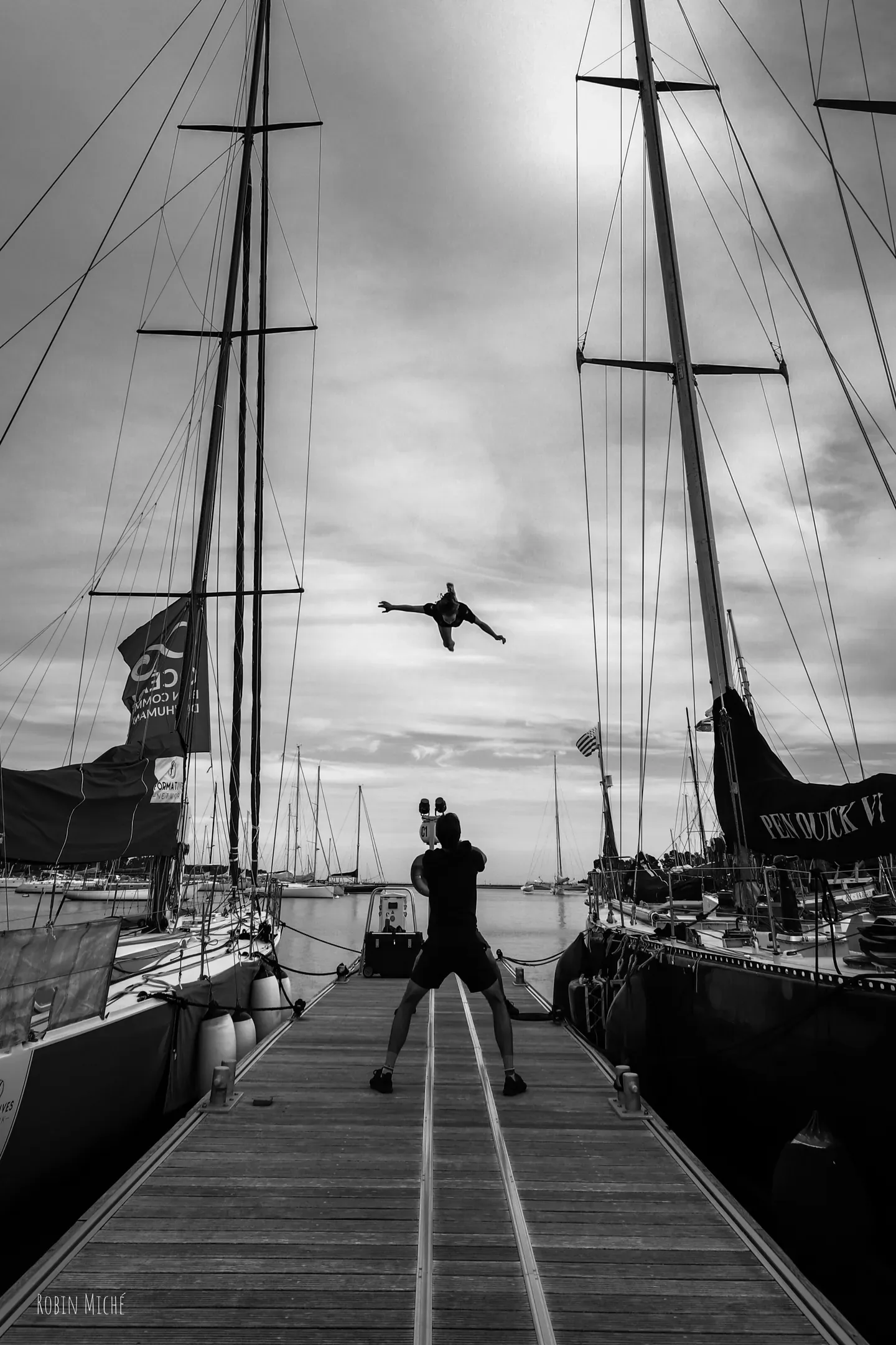 Ponton entre deux grands voiliers, un oiseau en vol au-dessus, en noir et blanc