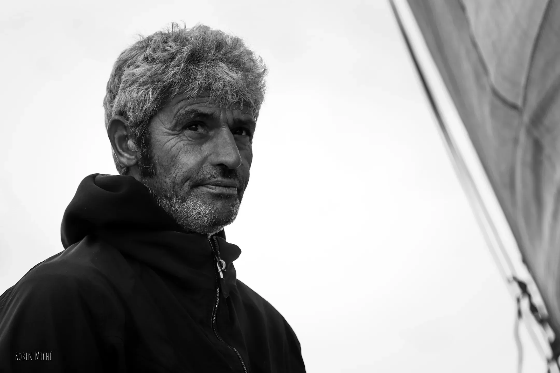 Portrait en noir et blanc d'un navigateur aux cheveux gris devant la voile