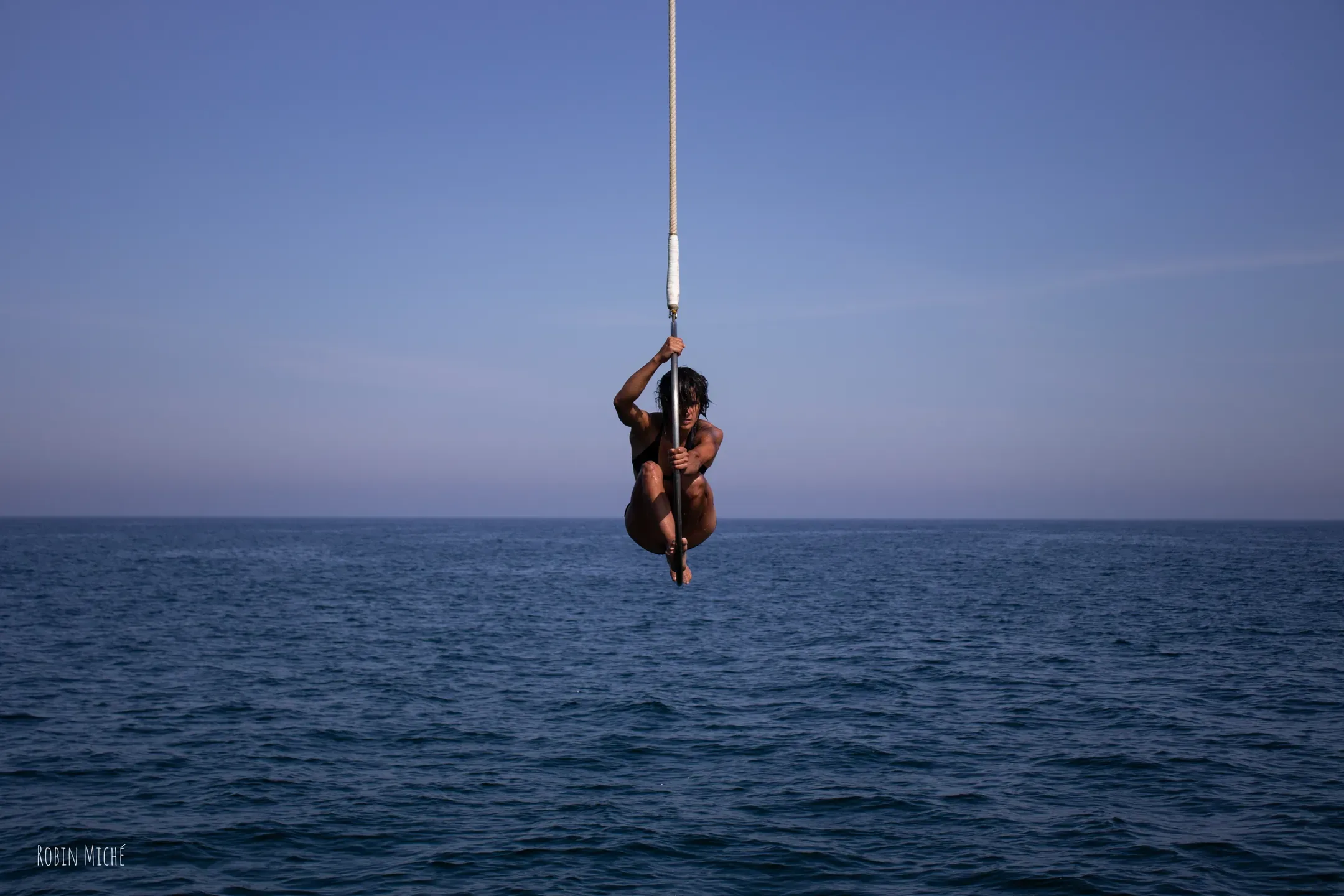 Funambule suspendu à une corde au-dessus de la mer, sous un ciel bleu