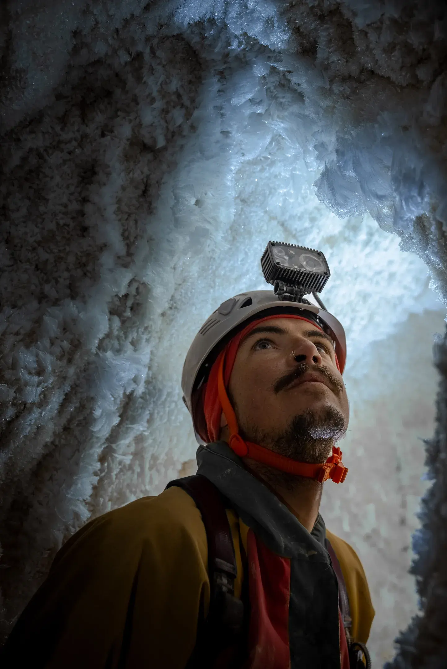 Spéléologue en combinaison rouge, la main posée sur une paroi de glace éclairée à la frontale
