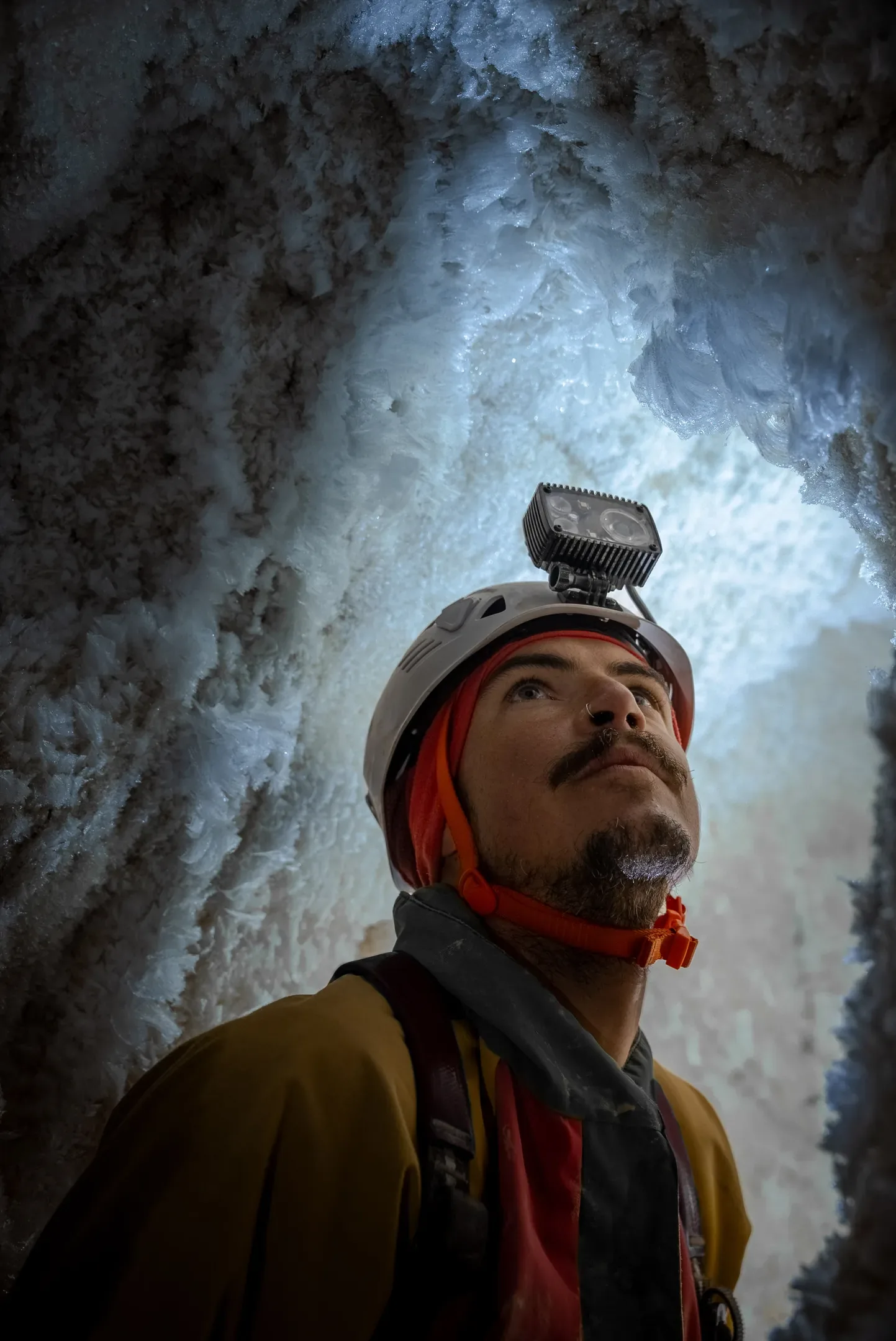 Portrait d'un spéléologue casqué, le regard levé vers la voûte de glace