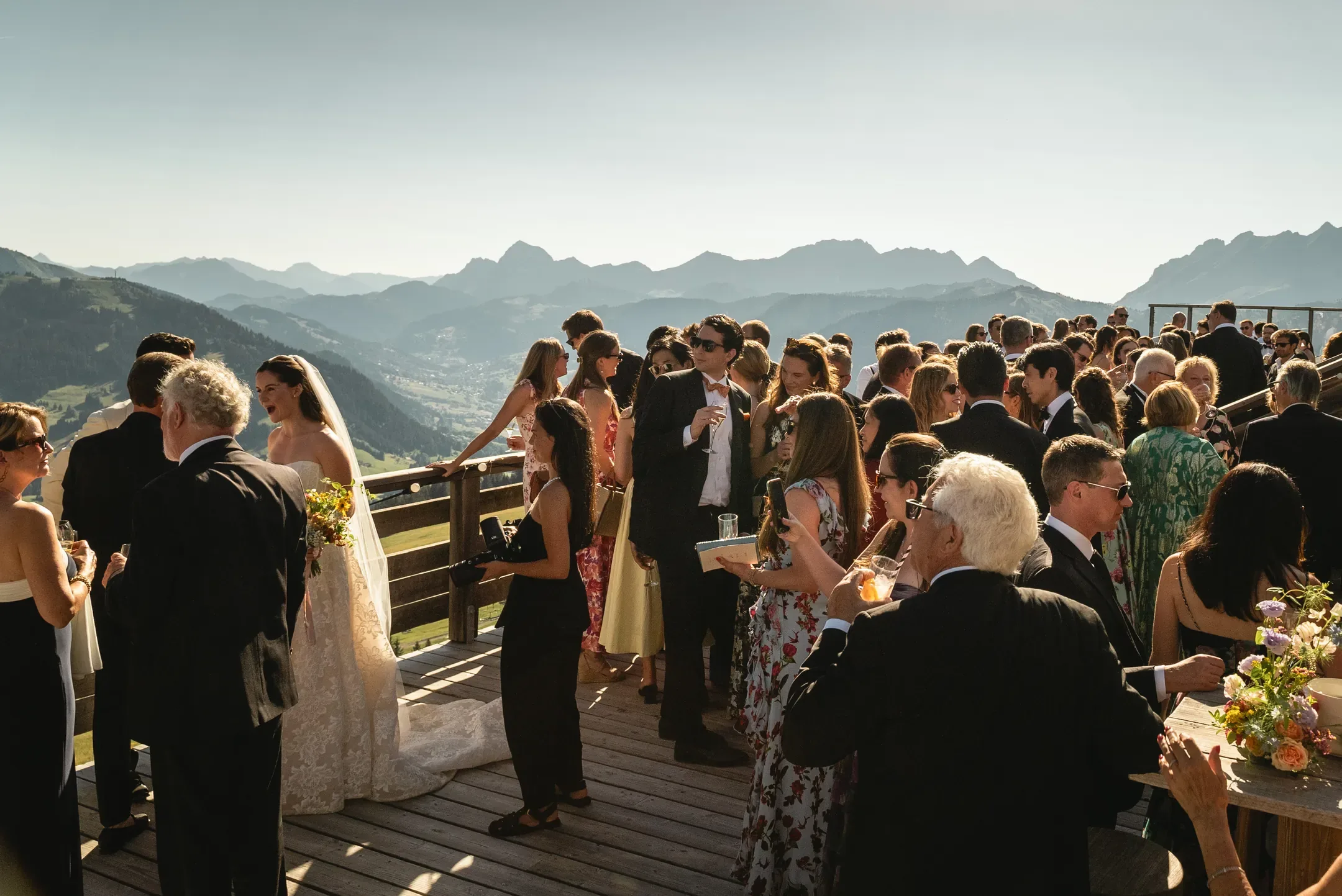 Invités réunis sur une terrasse au soleil couchant, montagnes en arrière-plan