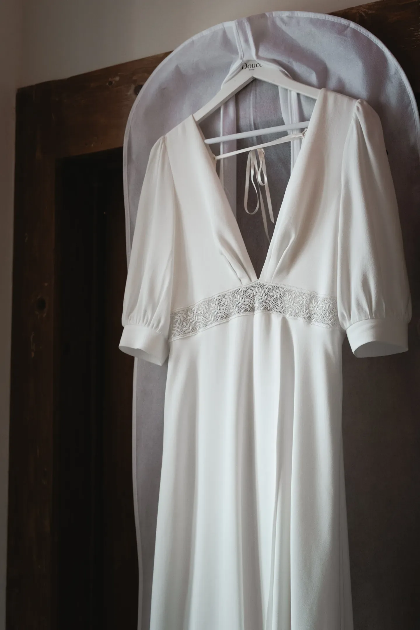 Robe de mariée blanche suspendue à un cintre dans l'encadrement d'une porte