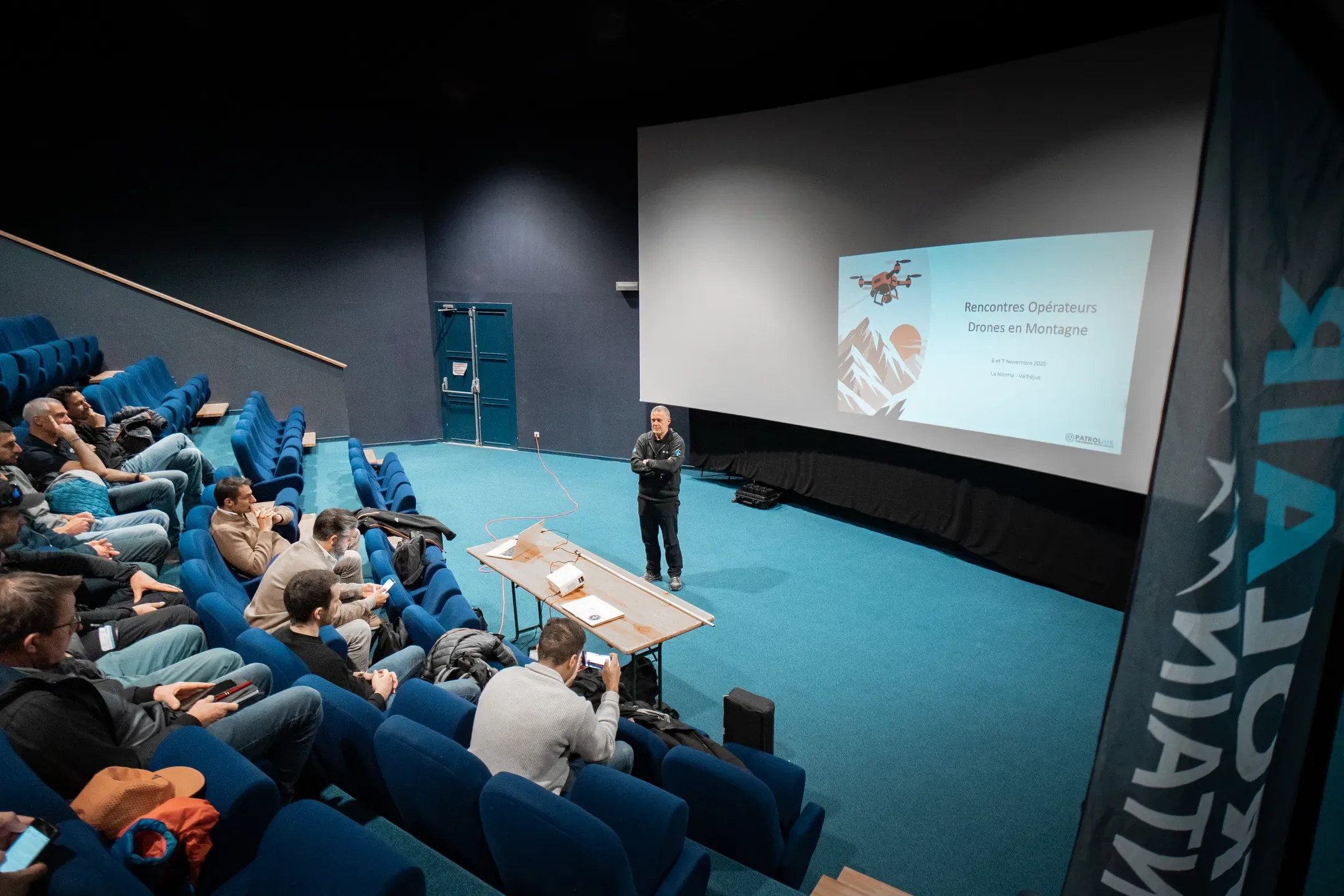 Auditorium aux fauteuils bleus face à un grand écran de présentation