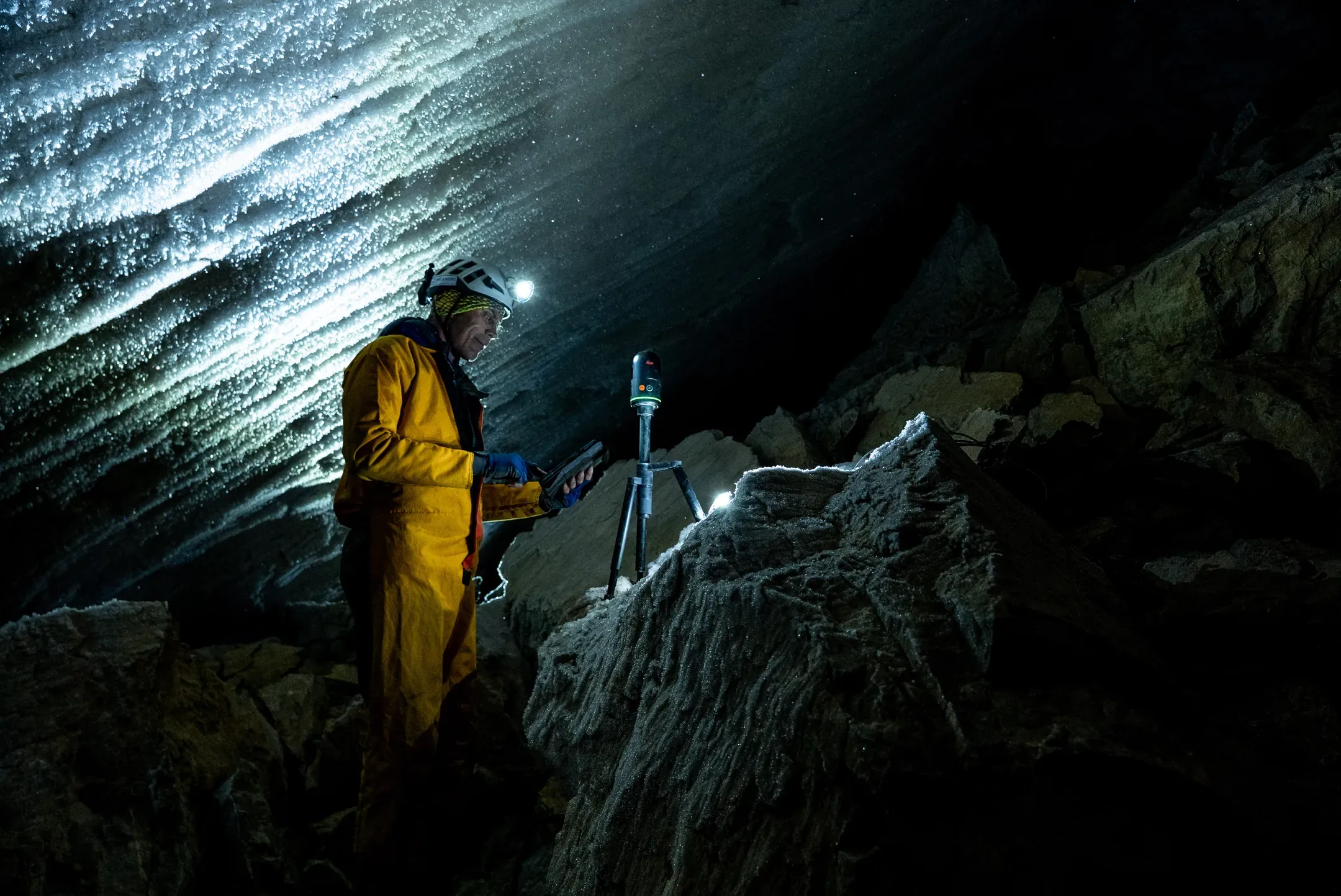 Spéléologue en combinaison jaune réalisant un relevé au scanner 3D dans la grotte