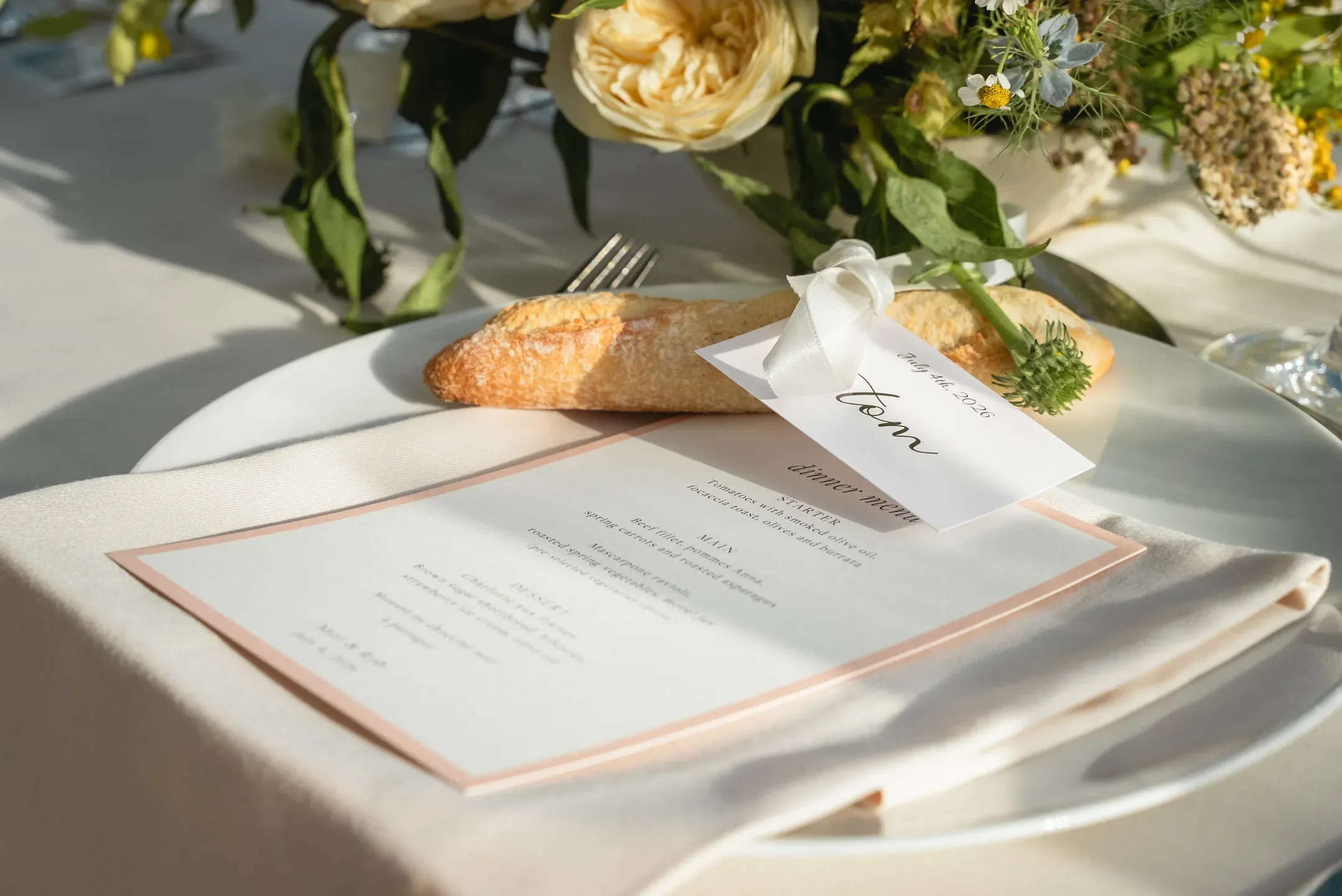 Assiette avec menu, carte au nom de l'invité et pain, entourée de fleurs